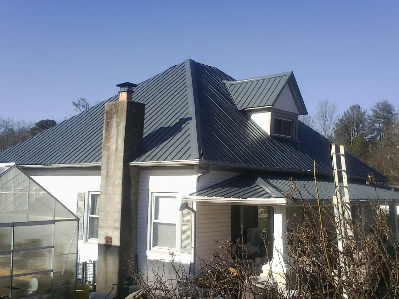 Dark blue standing seam metal roof on a white farmhouse with dormer — Slate & Tile Roof Repair by Roofing Brothers in Sulphur Springs