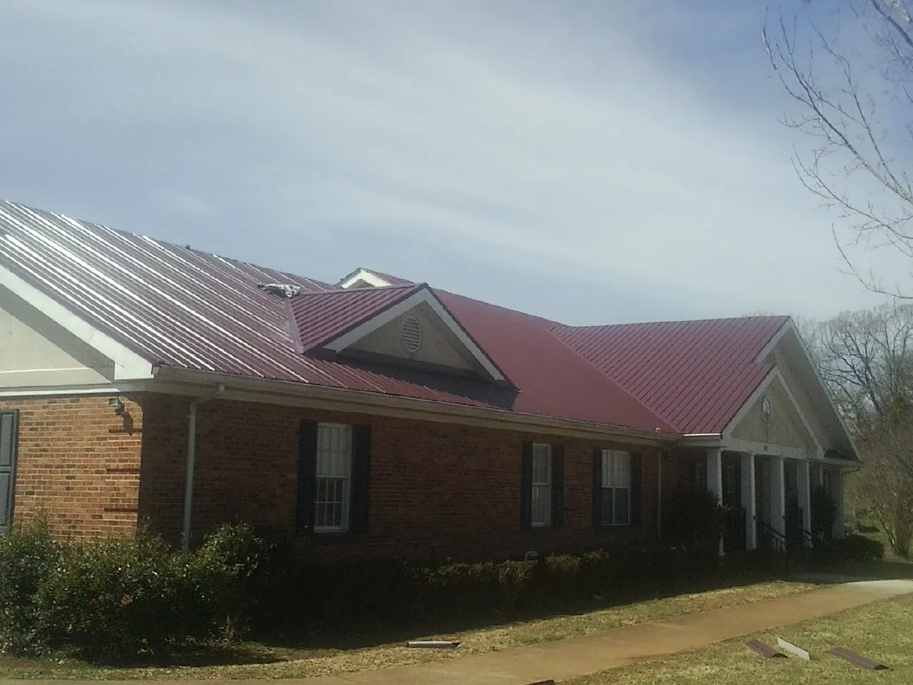 Red metal roof with gabled entries on a long brick building, from a Hail Damage Roof Repair job in Sulphur Springs