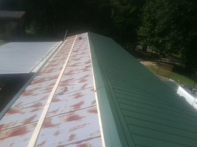 Old rusted panels beside newly installed green metal roofing — Wind Damage Roof Repair by Roofing Brothers in Sulphur Springs
