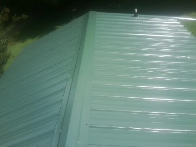 New green metal panels meeting at the ridge of a roof — Flat Roof Repair work by our crew in Sulphur Springs