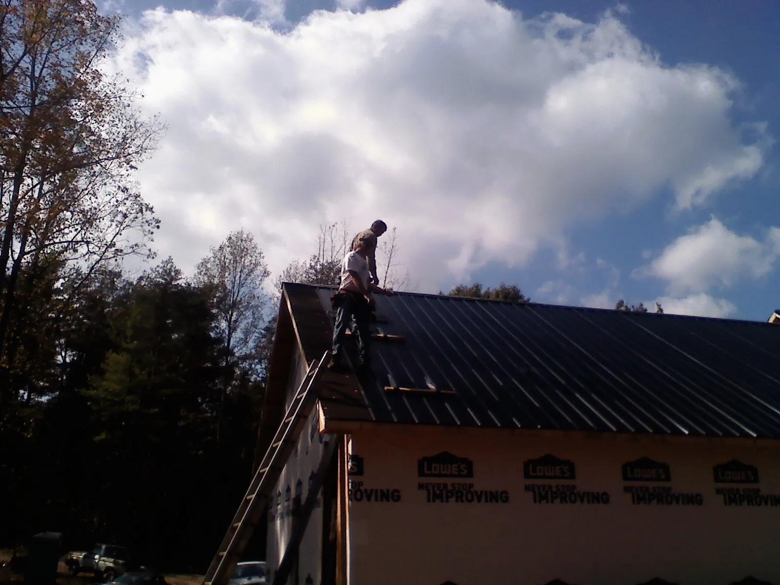 Roofer fastening dark metal panels high against a cloudy sky, from a Roof Inspection job in Sulphur Springs