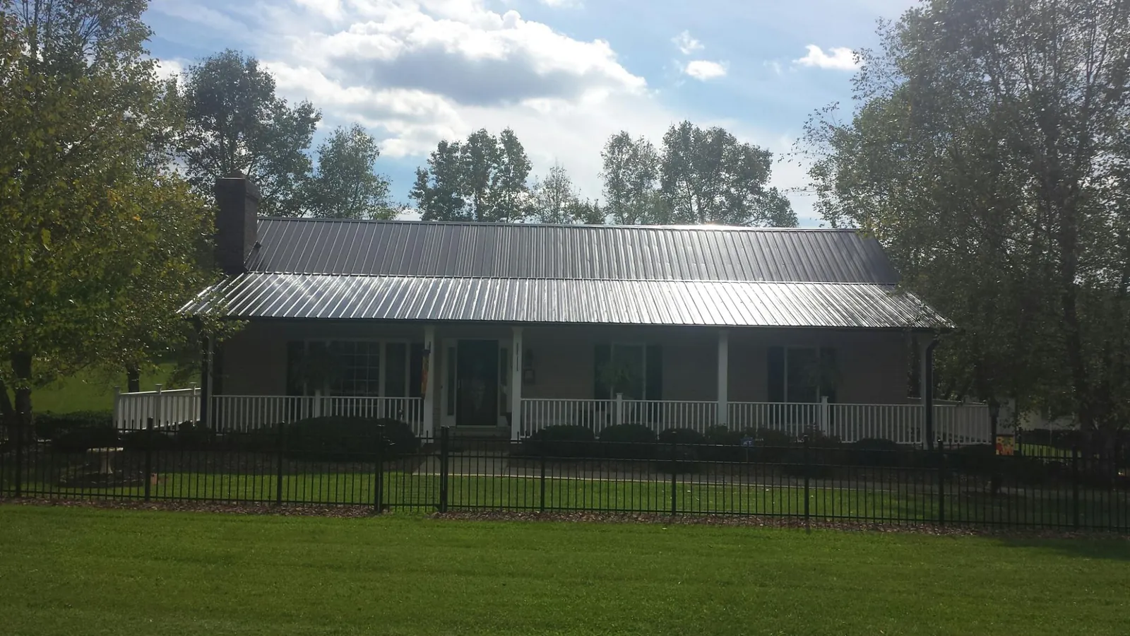 Gray metal roof on a brick ranch with a full width front porch — Gutter Guard Installation work by our crew in Sulphur Springs
