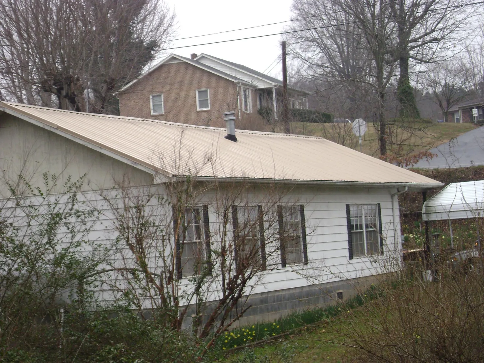 Tan metal roof on a white sided house set into a hillside — Commercial Roofing by Roofing Brothers in Sulphur Springs