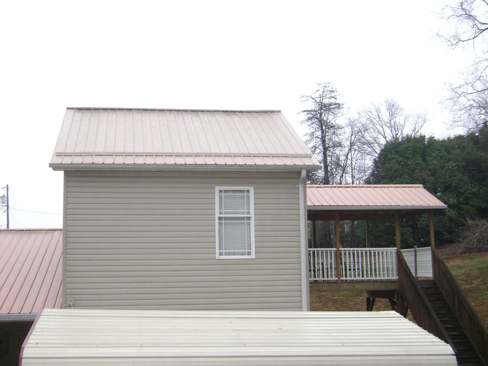 Tan metal roofs on a two story addition and attached porch, from a Roof Replacement job in Sulphur Springs